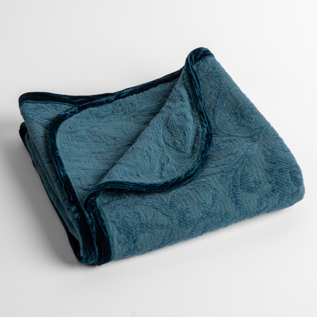 Cenote: a folded blanket with the corner turned down to show the trim against a white background, shot from an overhead angle.