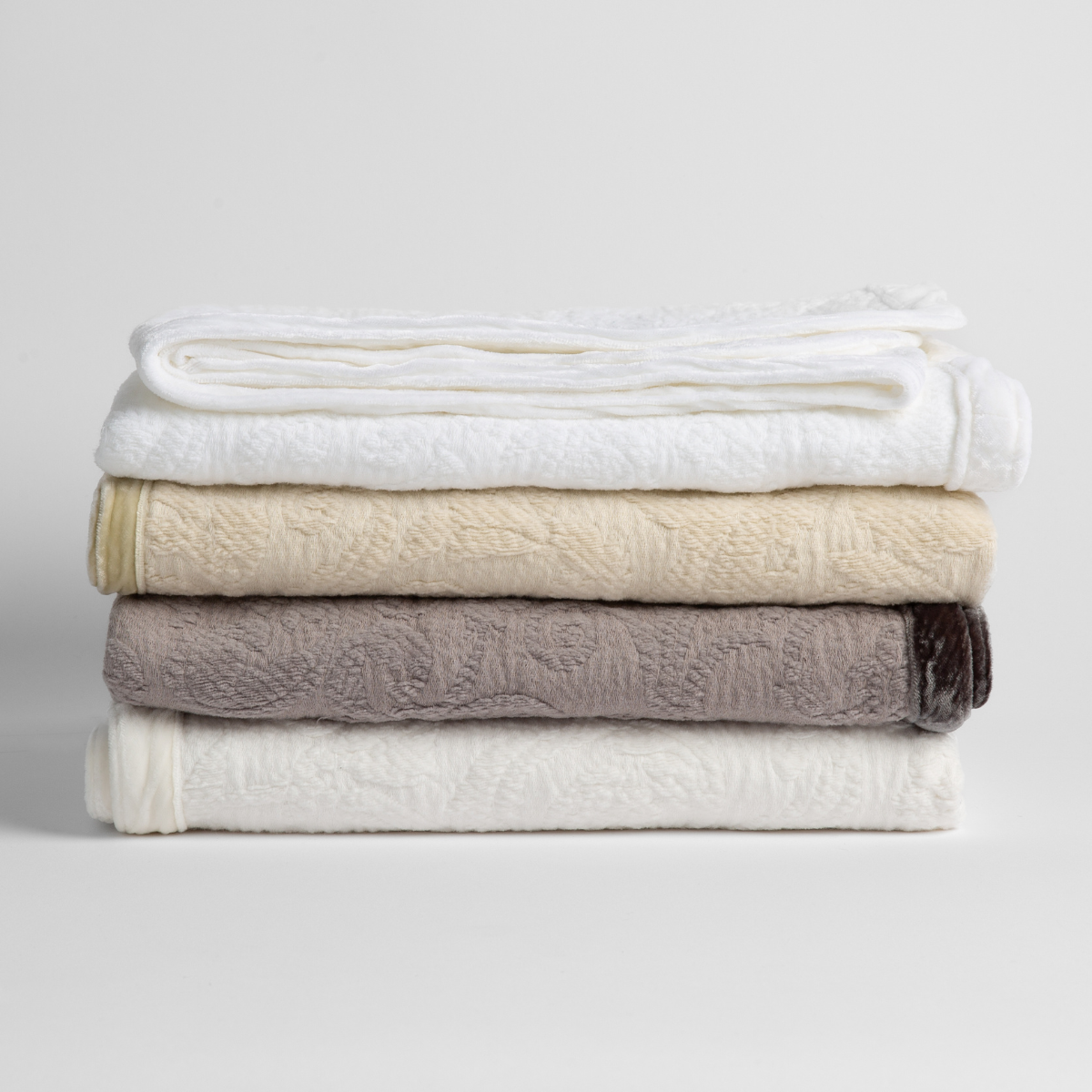 : a stack of four organic cotton baby blankets in white, parchment, moonlight and winter white. against a white background.