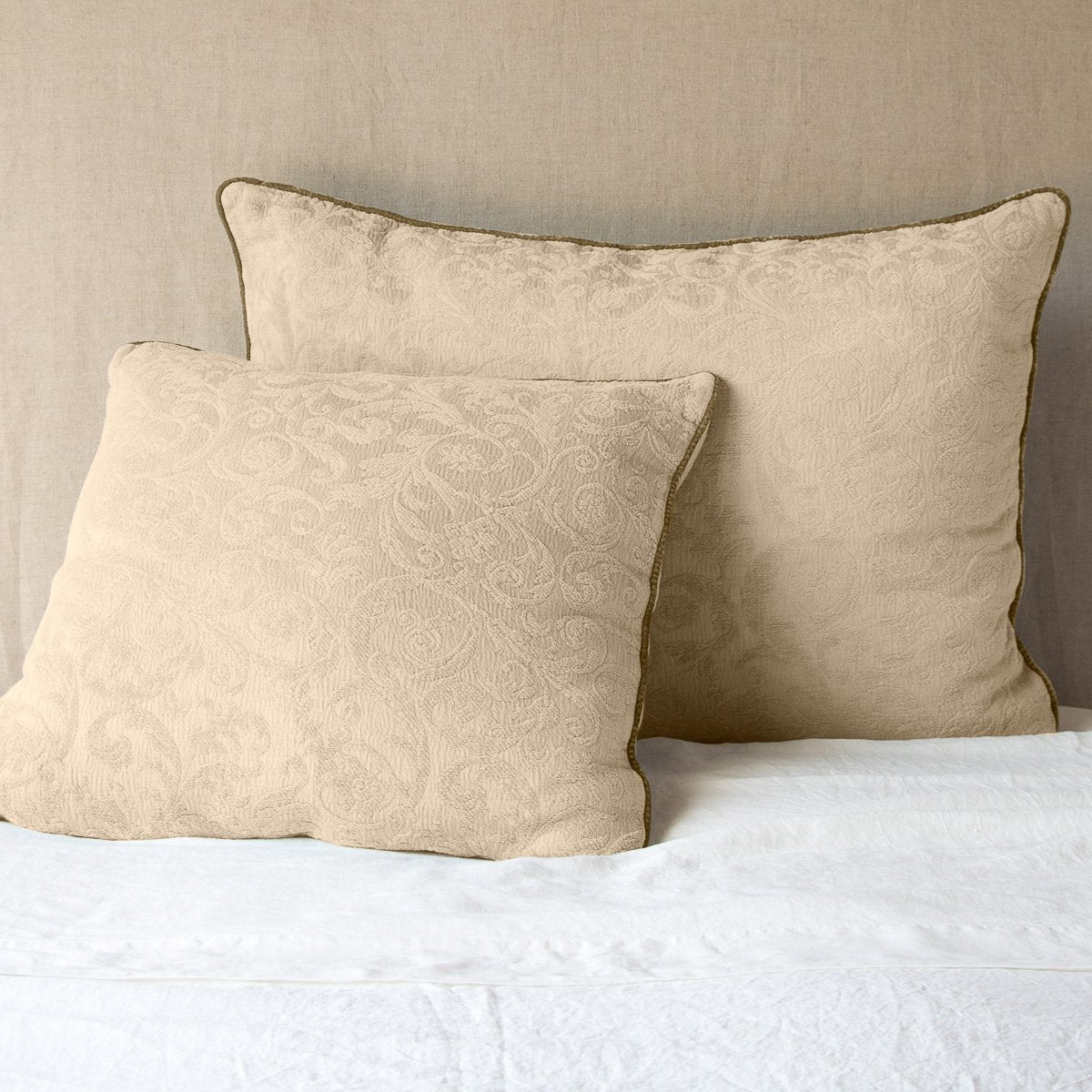 Honeycomb: Two Adele shams, shown in euro and deluxe sizes, leaning against a neutral toned headboard on white bedding.