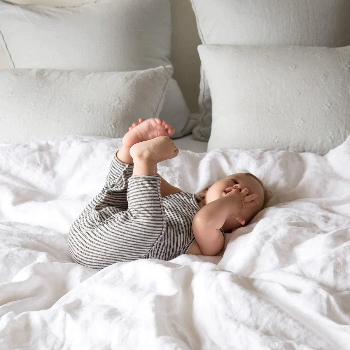 : Baby laying in a playful pose on a rumpled bed with Austin shams in the background.