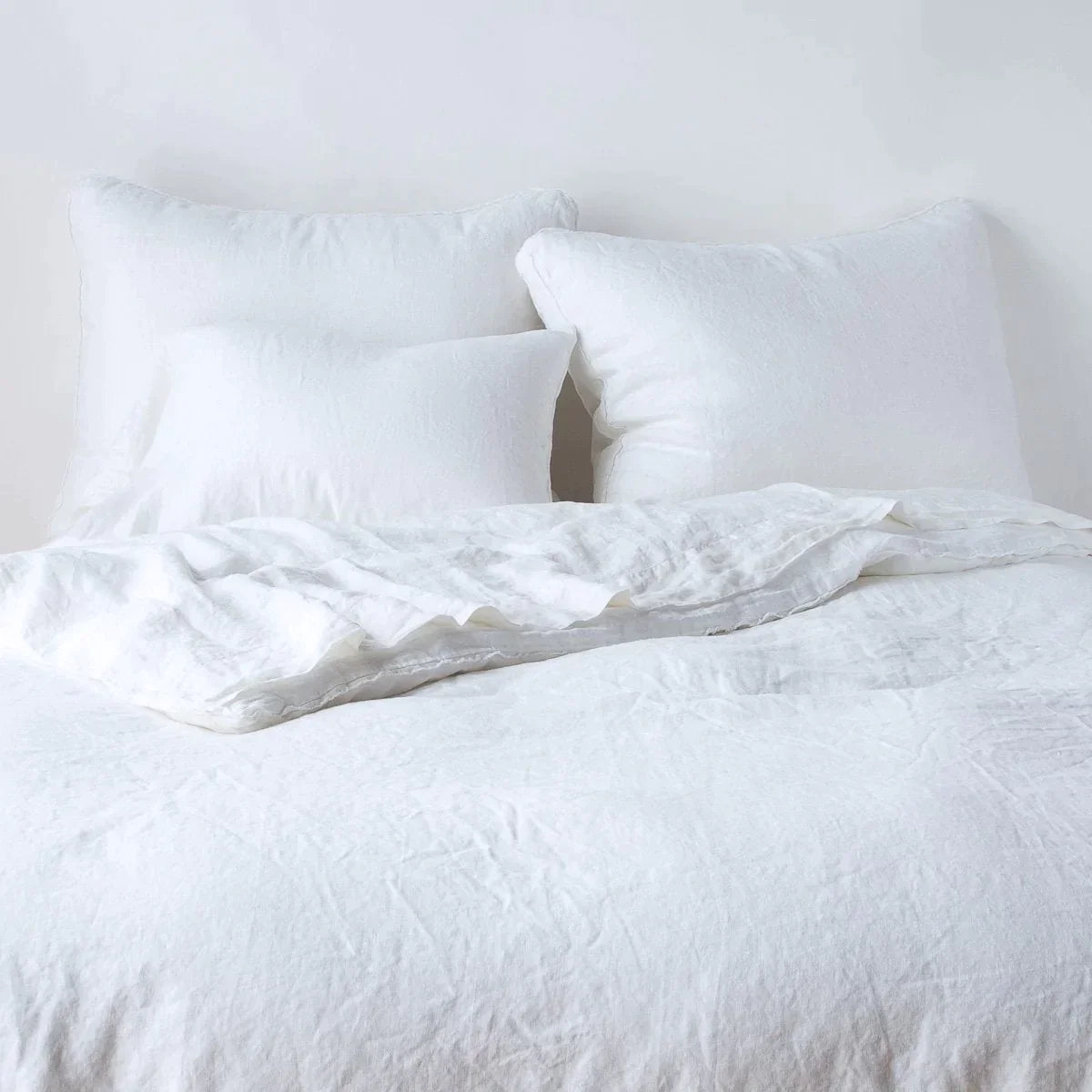White: Midweight linen shams shown from foot of bed, leaning against a plain background with monochromatic bedding.