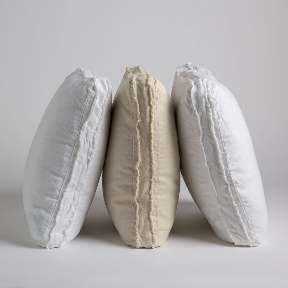 : three midweight linen throw pillows leaning on one another upright. Pillows shown in white, parchment and winter white.