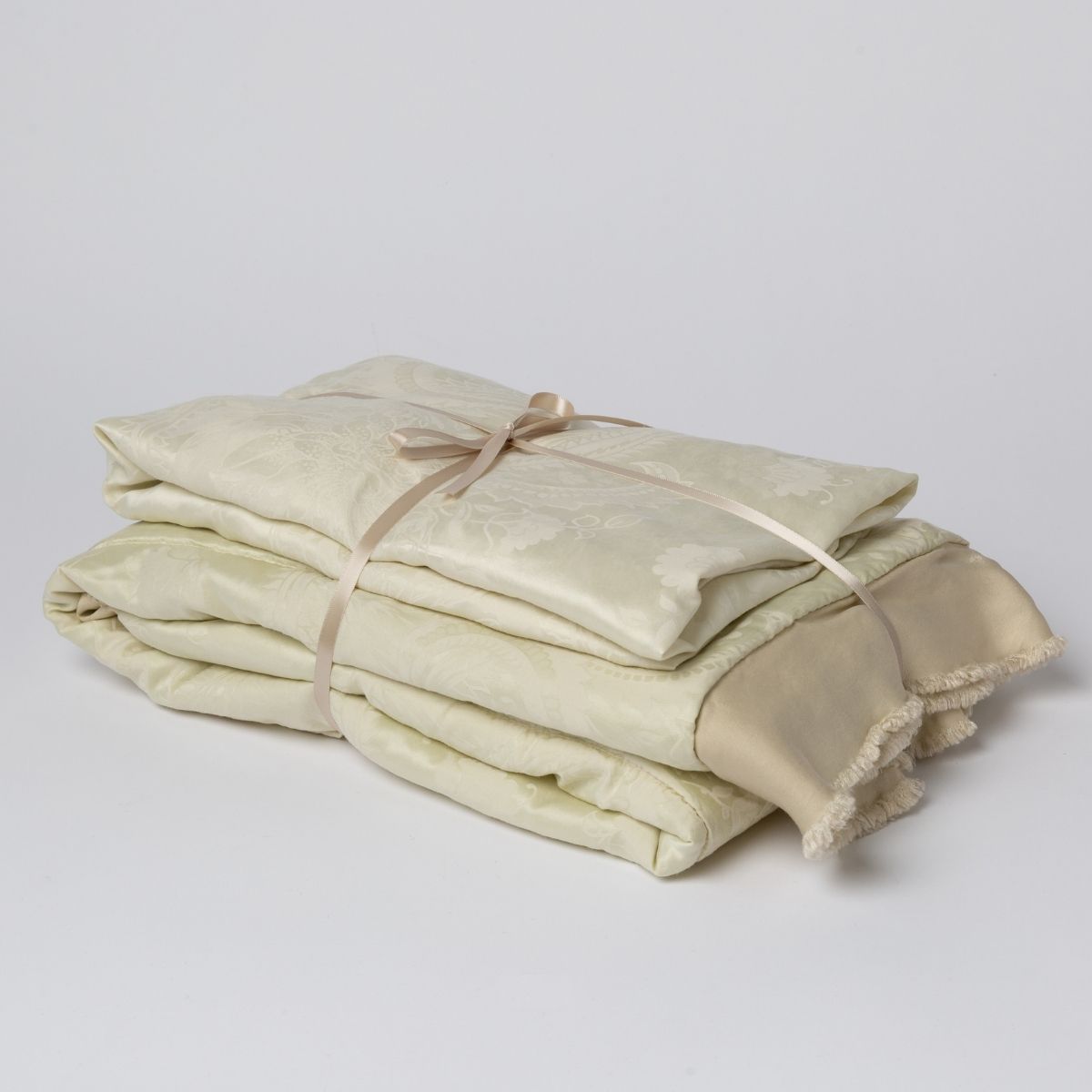 Parchment: matching crib sheet and baby blanket bundled and tied with a ribbon against a white background.
