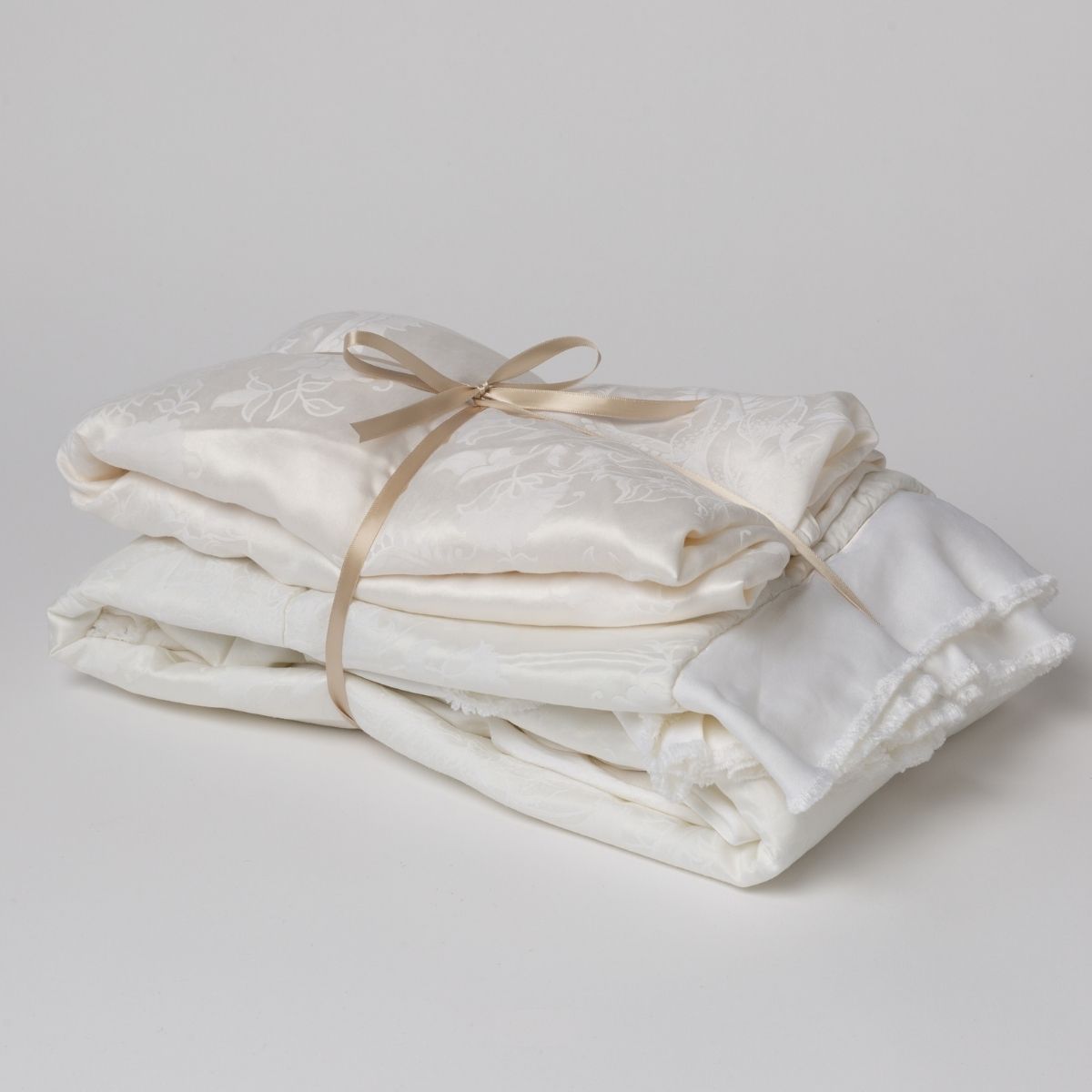 White: matching crib sheet and baby blanket bundled and tied with a ribbon against a white background.