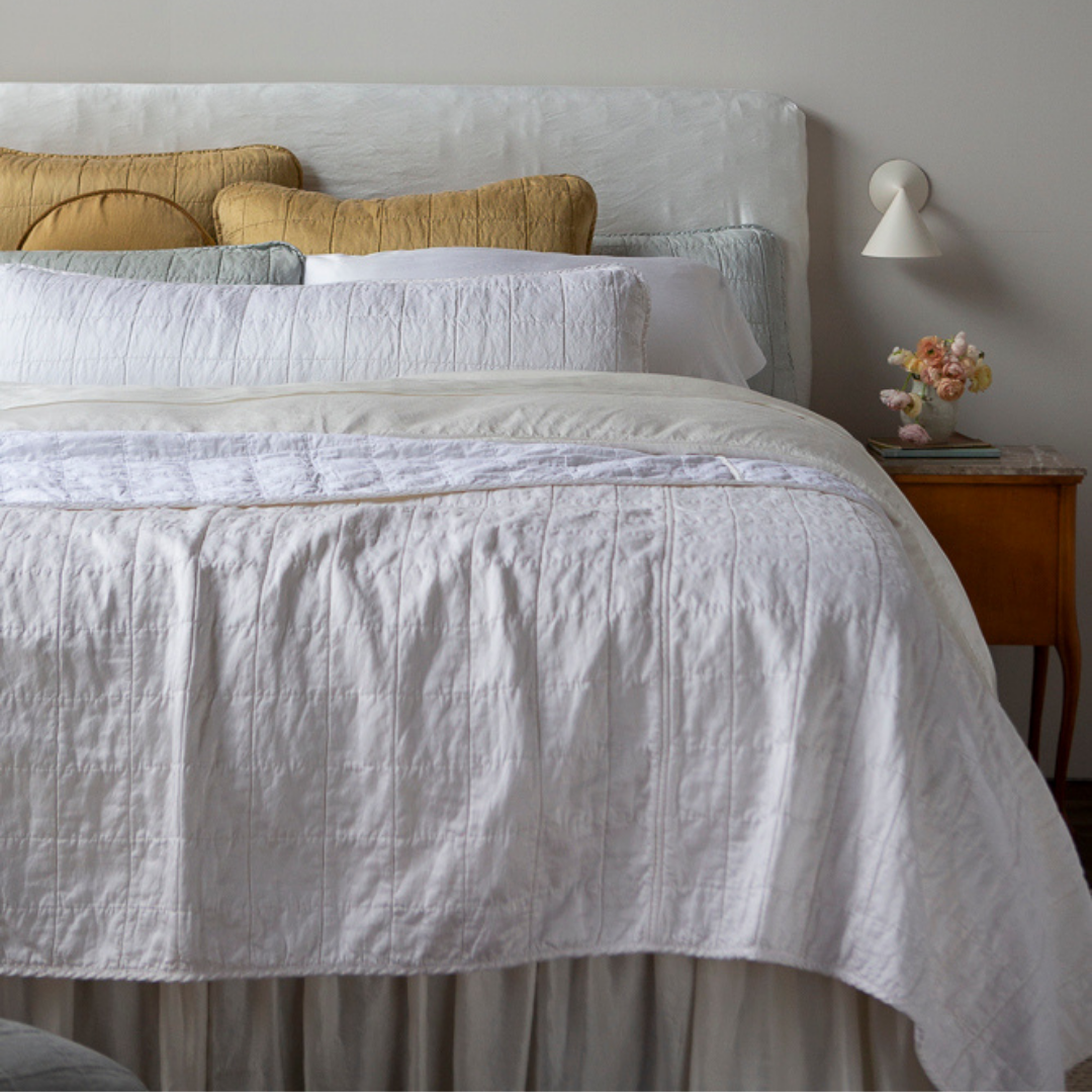 : a quilted charmeuse coverlet layered over a duvet cover and sheets - shown from the foot of the bed with the coverlet folded back shows the cotton sateen back and how it takes the dye differently than its front.