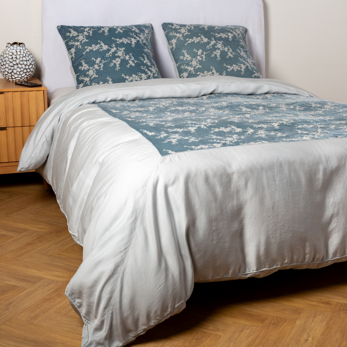 Cloud: A ¾ angle shot of an embroidered silk velvet and tencel duvet cover and matching shams with a vase and cell phone on the side table.