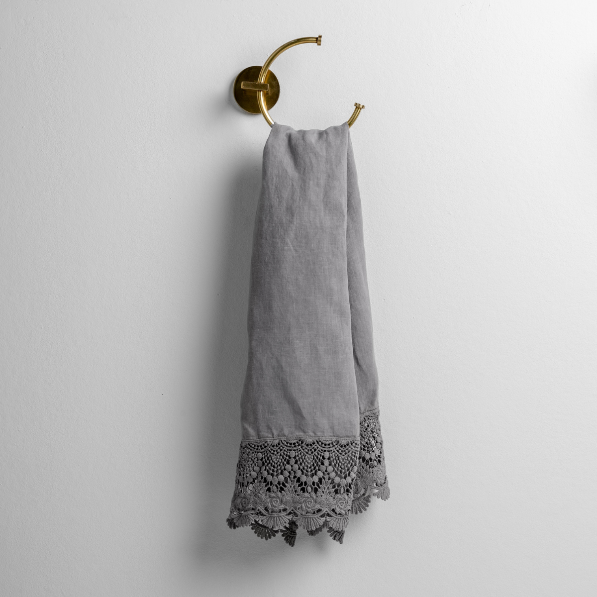Moonlight: linen with mattine lace trimmed guest towel on a decorative towel ring mounted on a white wall.