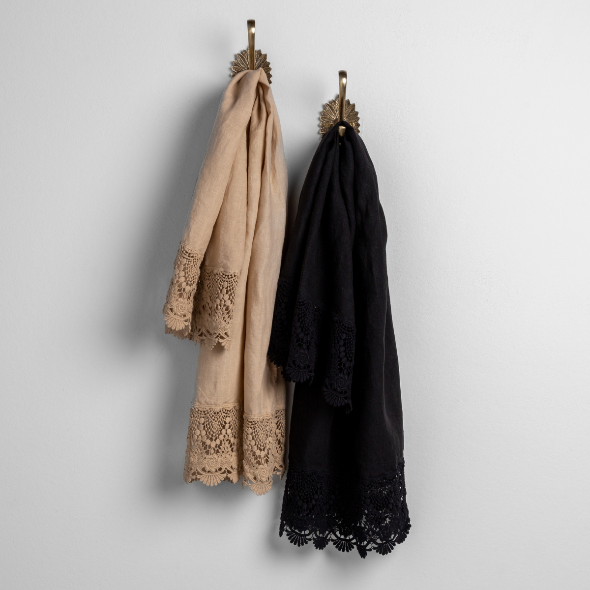 : lace trimmed linen guest towels in honeycomb and corvino hanging from decorative towel hooks against a plain white wall.