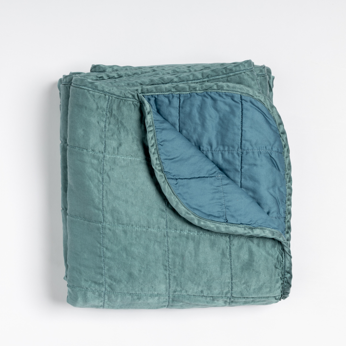 Cenote: an overhead shot of a quilted charmeuse blanket in cenote, a vibrant ocean-inspired blue-green, with a corner folded down, showing its cotton sateen back.