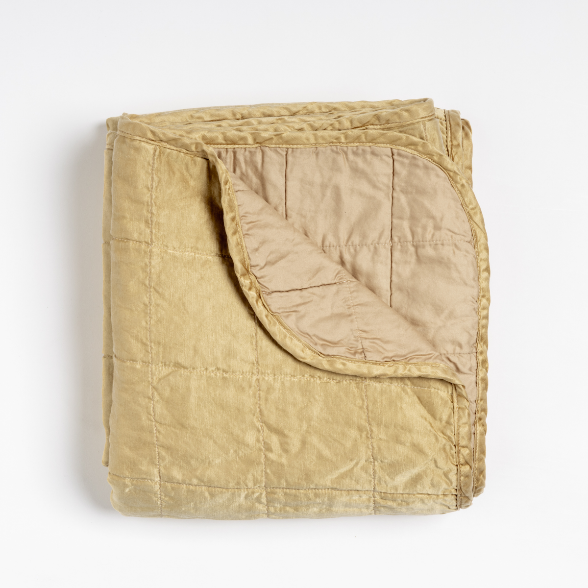 Honeycomb: an overhead shot of a quilted charmeuse blanket in honeycomb, a warm golden tone, with a corner folded down, showing its cotton sateen back.