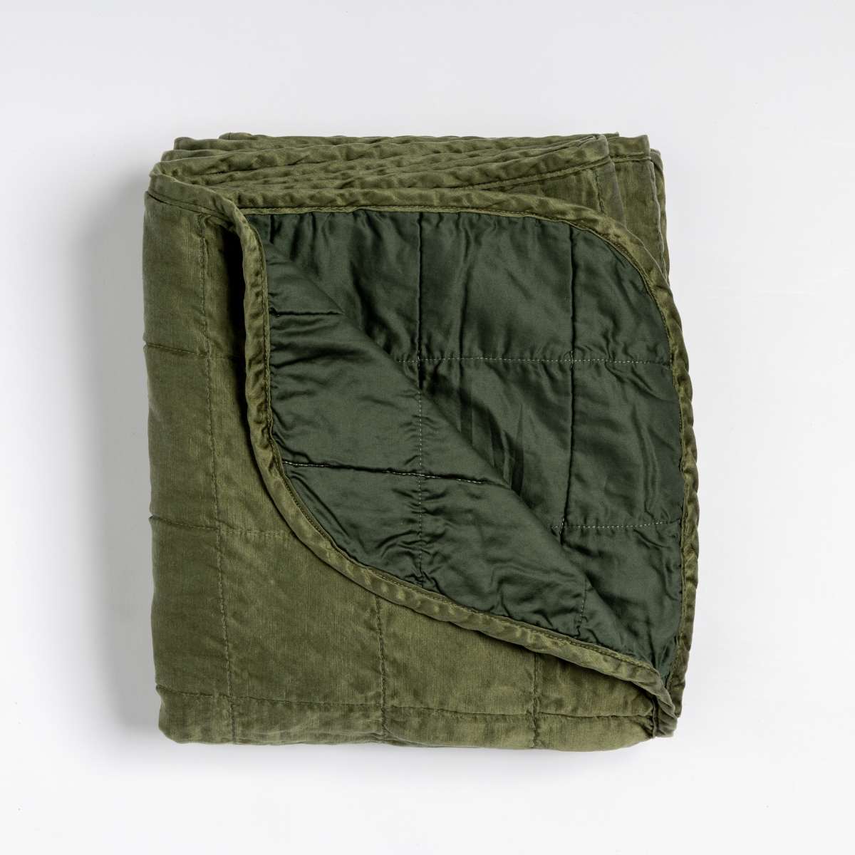 Juniper: an overhead shot of a quilted charmeuse blanket in juniper, a deeply saturated dark green, with a corner folded down, showing its cotton sateen back.