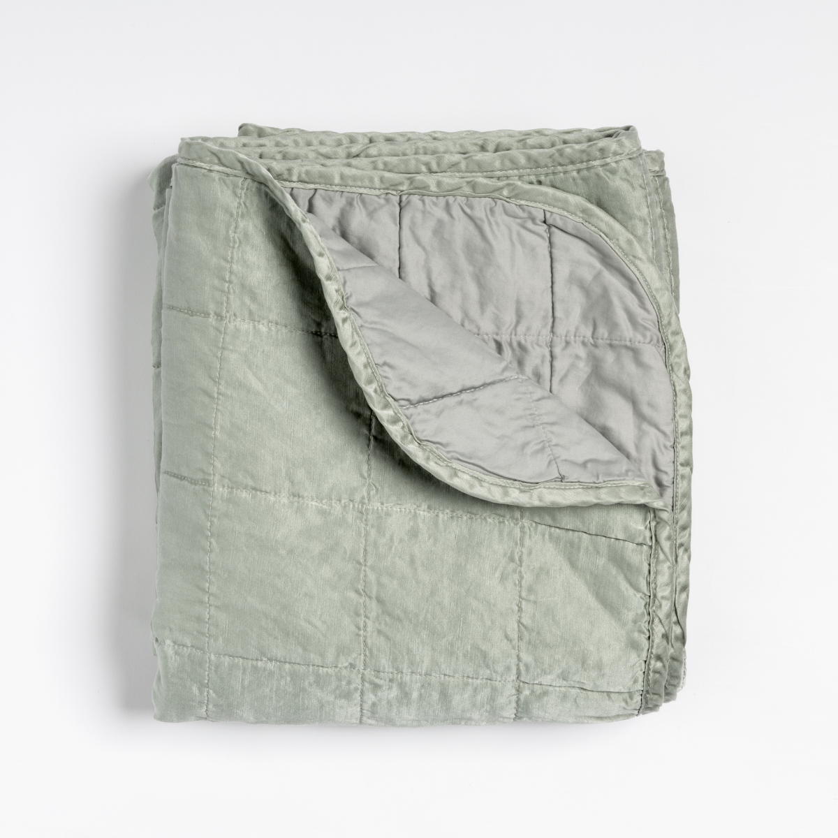 Mineral: an overhead shot of a quilted charmeuse blanket in mineral, a soothing seafoam blue with subtle grey-green undertones, with a corner folded down, showing its cotton sateen back.
