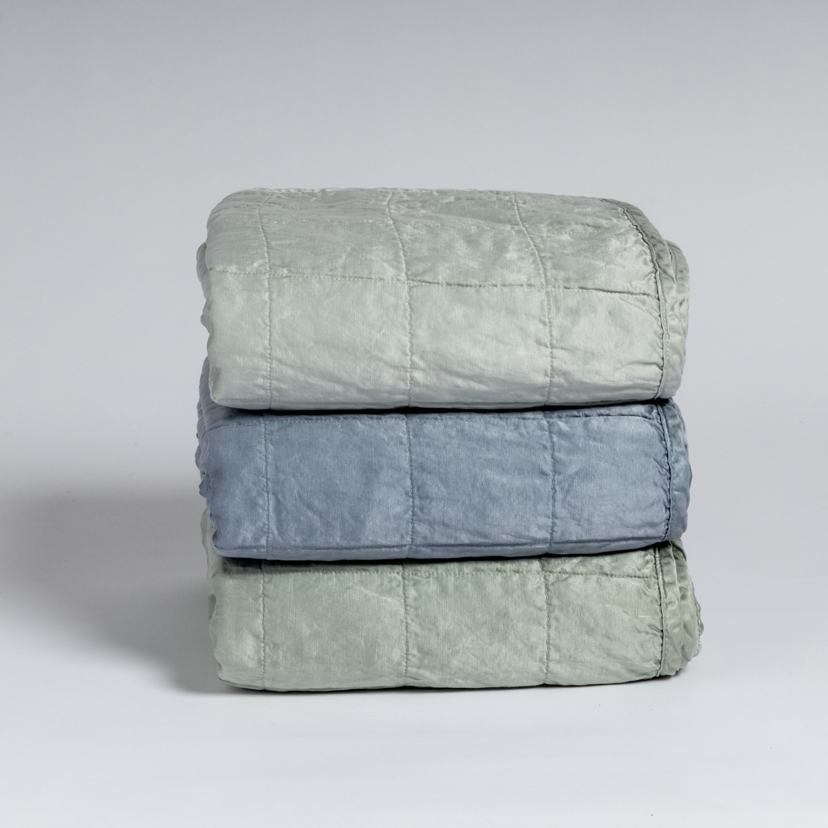 : A stack of three square-quilted charmeuse blankets shot straight on against a white background.