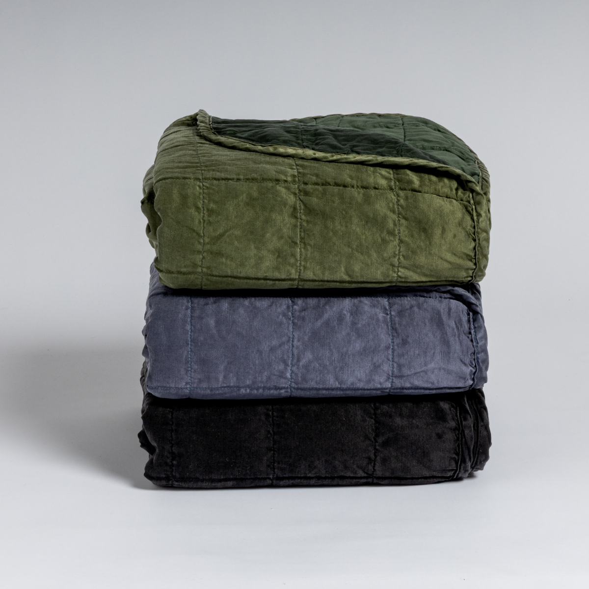 A stack of three square-quilted charmeuse blankets shot straight on against a white background.