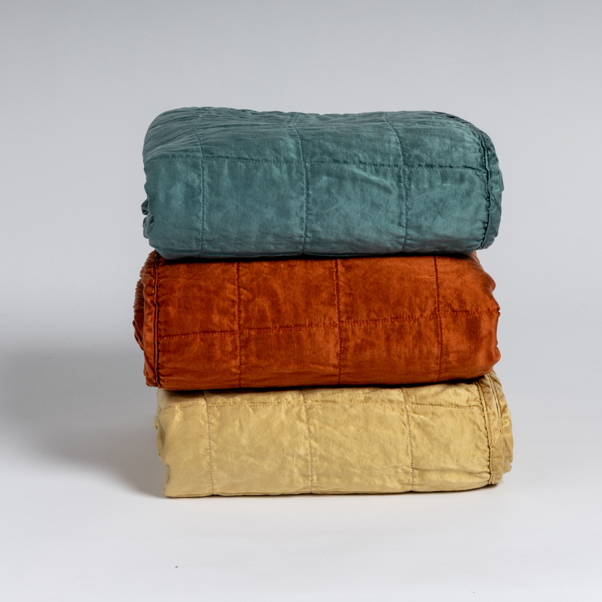 A stack of three square-quilted charmeuse blankets shot straight on against a white background.