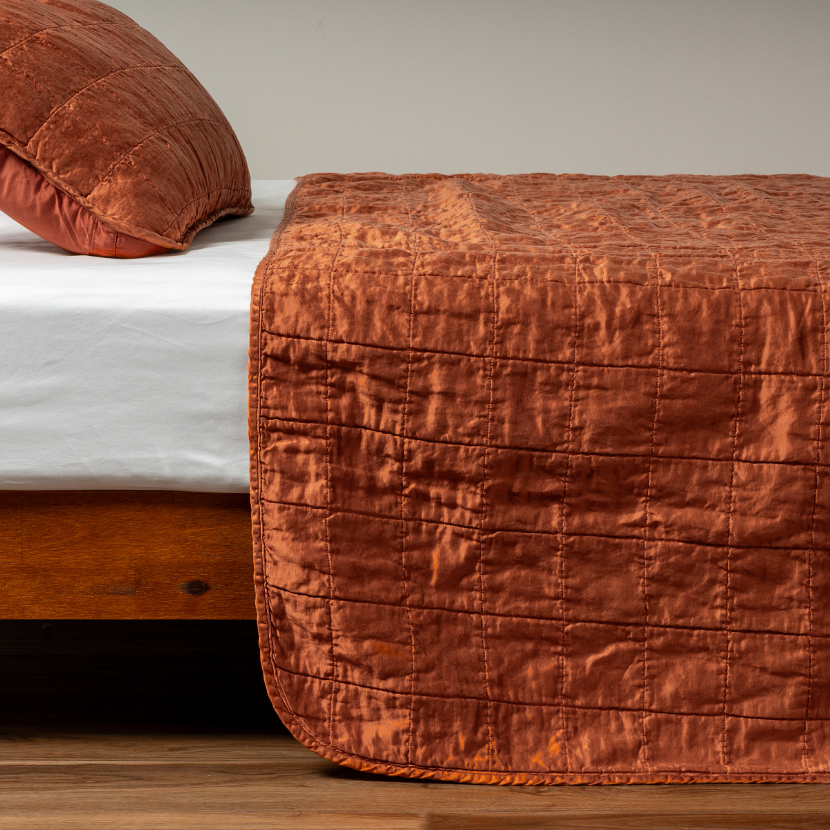 Autumn: A side shot of a square quilted charmeuse coverlet in autumn, a rich terracotta tone, with its matching sham.