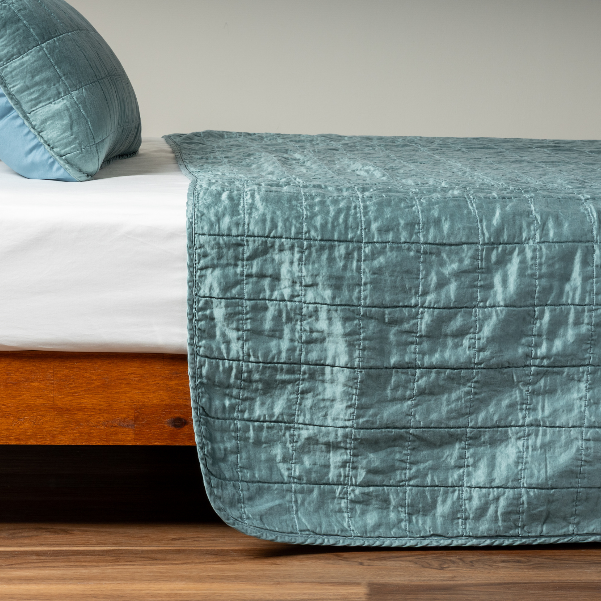 Cenote: A side shot of a square quilted charmeuse coverlet in cenote, a vibrant ocean-inspired blue-green, with its matching sham.