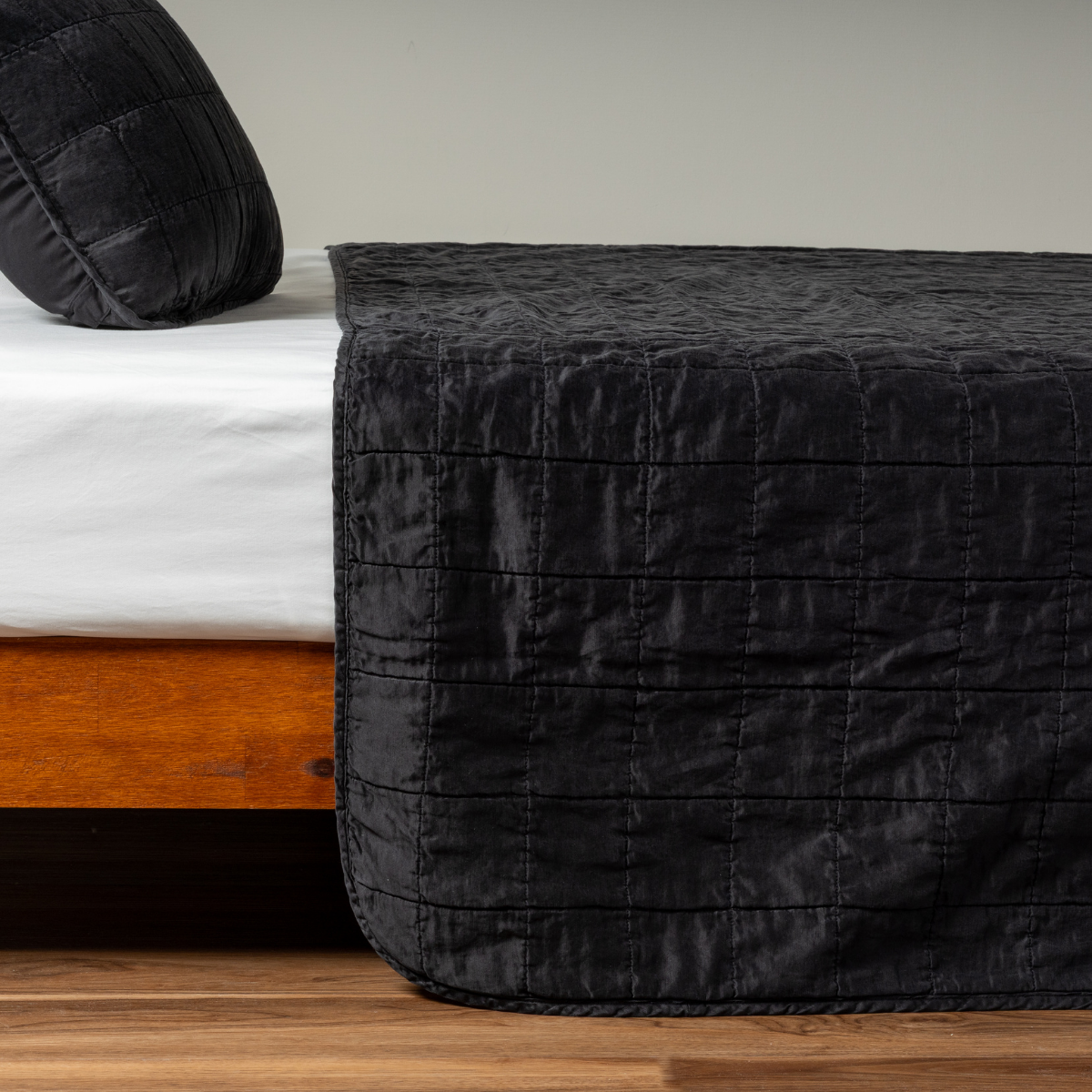 Corvino: A side shot of a square quilted charmeuse coverlet in corvino, a classic black, with its matching sham.