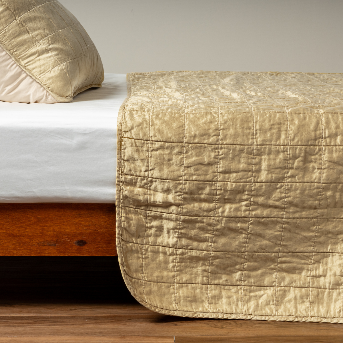 Honeycomb: A side shot of a square quilted charmeuse coverlet in honeycomb, a warm golden tone, with its matching sham.