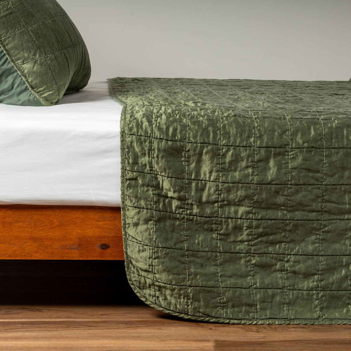 Juniper: A side shot of a square quilted charmeuse coverlet in juniper, a deeply saturated dark green, with its matching sham.