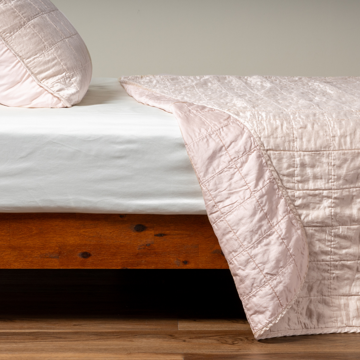 Pearl: A side shot of a square quilted charmeuse coverlet in pearl, a soft rose pink tone, with its matching sham, the corner of the coverlet peeled back, revealing the cotton sateen back.