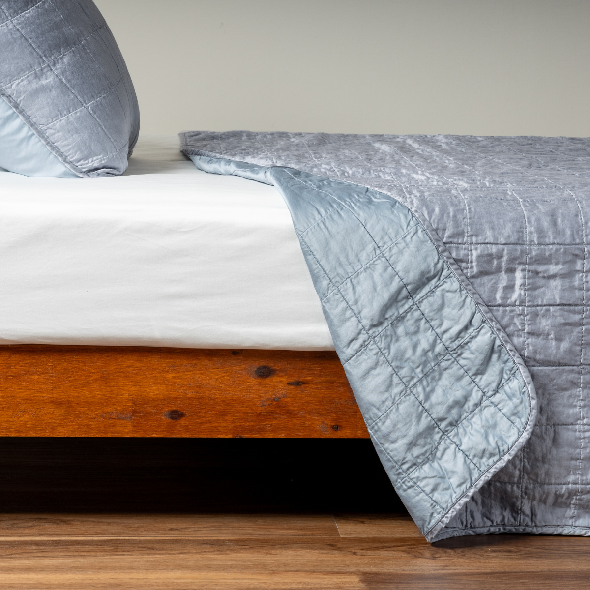 Tahoe Blue: A side shot of a square quilted charmeuse coverlet in tahoe blue, a crisp true blue, with its matching sham, the corner of the coverlet peeled back, revealing the cotton sateen back.