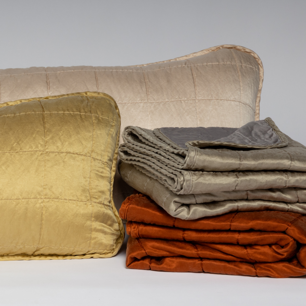 : A cluster shot of square-quilted throw pillows and blankets shown against a white background.