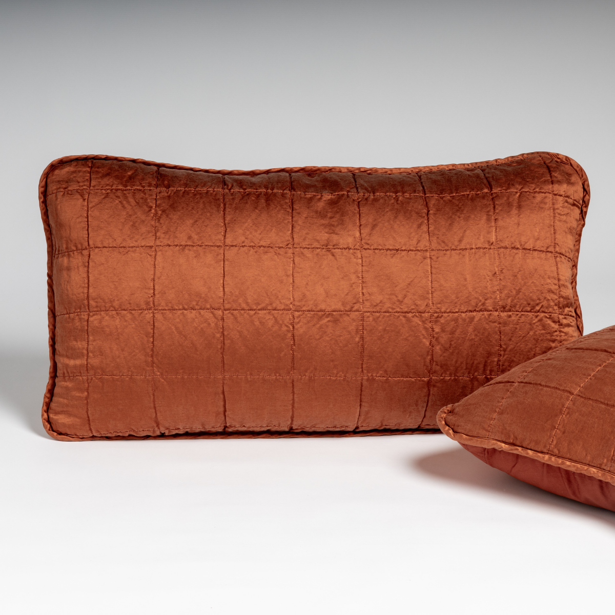 Autumn: A pair of shams in autumn, a rich terracotta tone, shown against a white background with one sham upright and the other on its side to show the cotton sateen back and square-quilted charmeuse front.