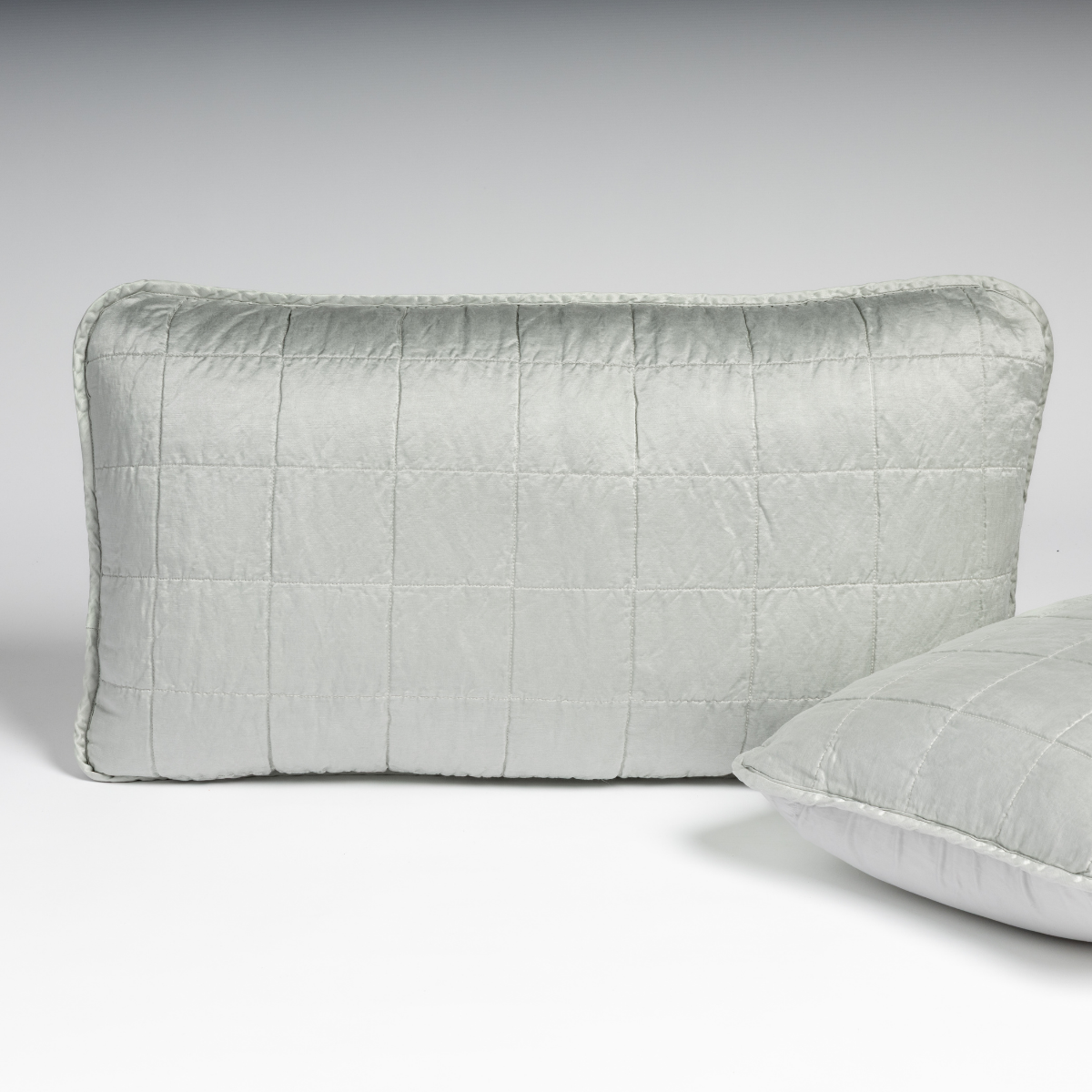 Cloud: A pair of shams in cloud, a subtle sky blue-grey, shown against a white background with one sham upright and the other on its side to show the cotton sateen back and square-quilted charmeuse front.