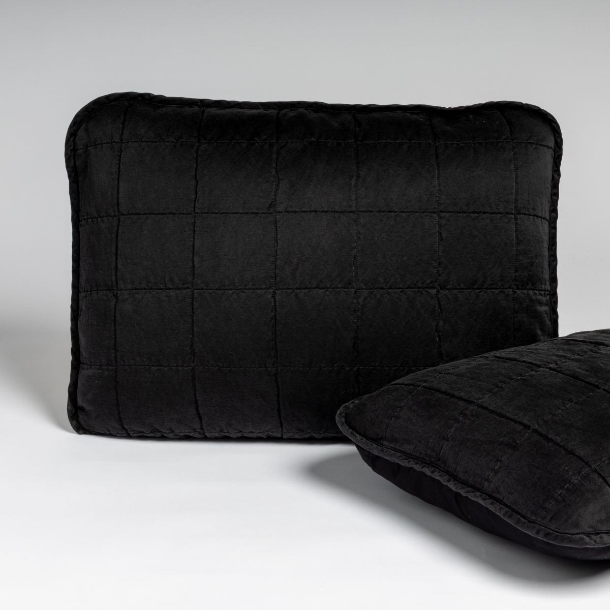 Corvino: A pair of shams shown in corvino, our classic black, against a white background with one sham upright and the other on its side to show the cotton sateen back and square-quilted charmeuse front.