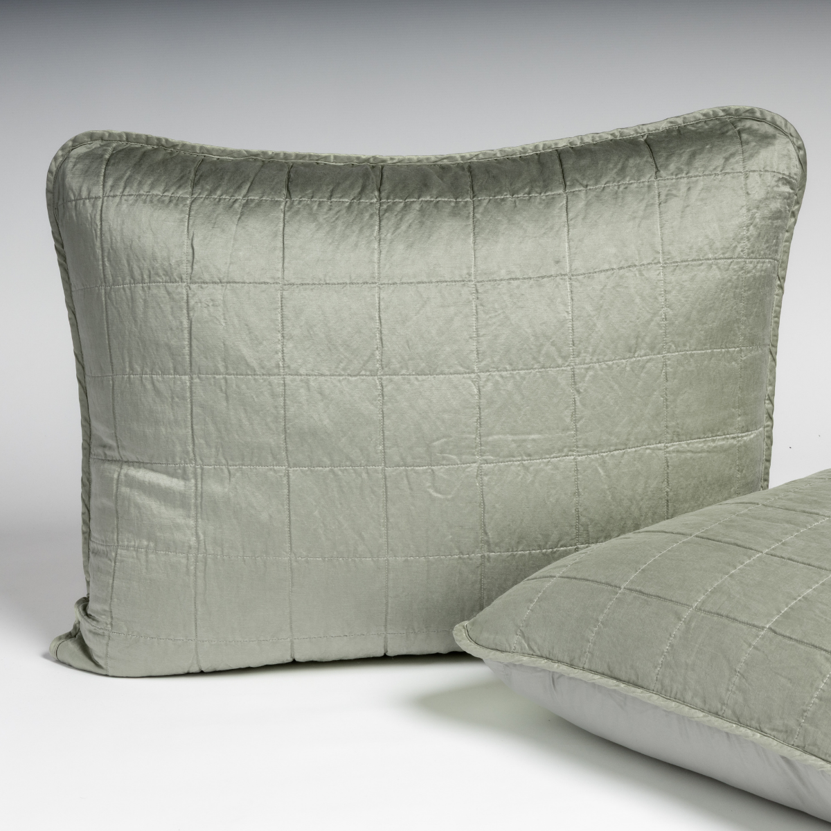 Eucalyptus: A pair of shams in eucalyptus, a soft light green, shown against a white background with one sham upright and the other on its side to show the cotton sateen back and square-quilted charmeuse front.