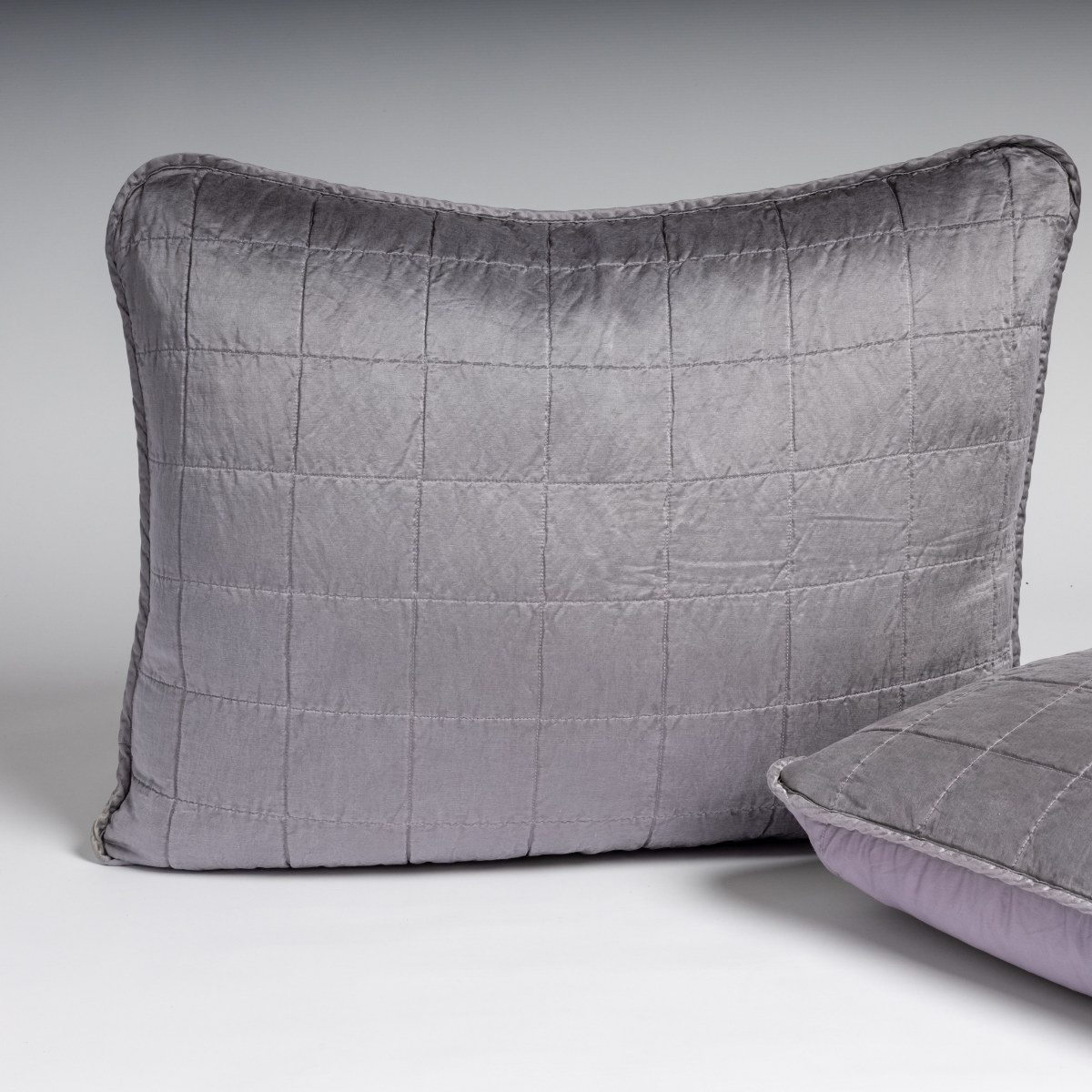 French Lavender: A pair of shams shown in french lavender, a neutral violet tone, against a white background with one sham upright and the other on its side to show the cotton sateen back and square-quilted charmeuse front.
