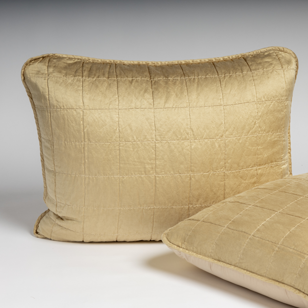 Honeycomb: A pair of shams in honeycomb, a warm golden tone, shown against a white background with one sham upright and the other on its side to show the cotton sateen back and square-quilted charmeuse front.