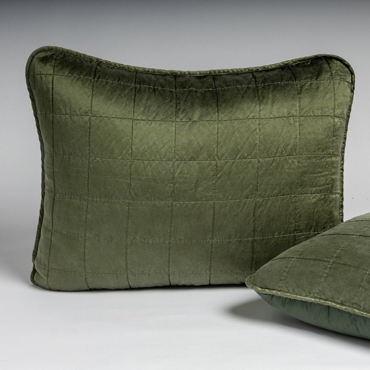 Juniper: A pair of shams in juniper, a deeply saturated dark green, shown against a white background with one sham upright and the other on its side to show the cotton sateen back and square-quilted charmeuse front.