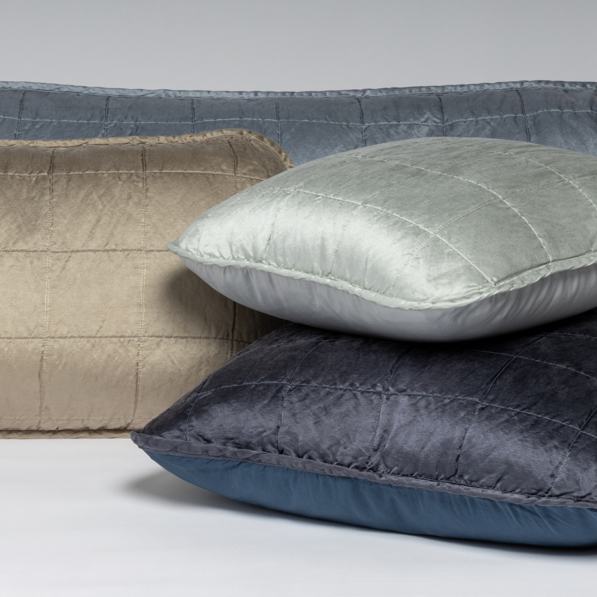 : A cluster shot of four square-quilted charmeuse shams showing their unquilted cotton sateen back.