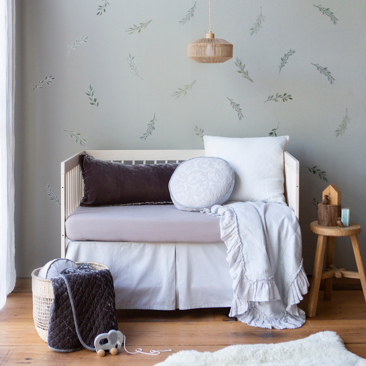 : Cotton sateen crib skirt in cloud shown on a crib in grey and light blue tones, highlighting the tailored, ungathered style.