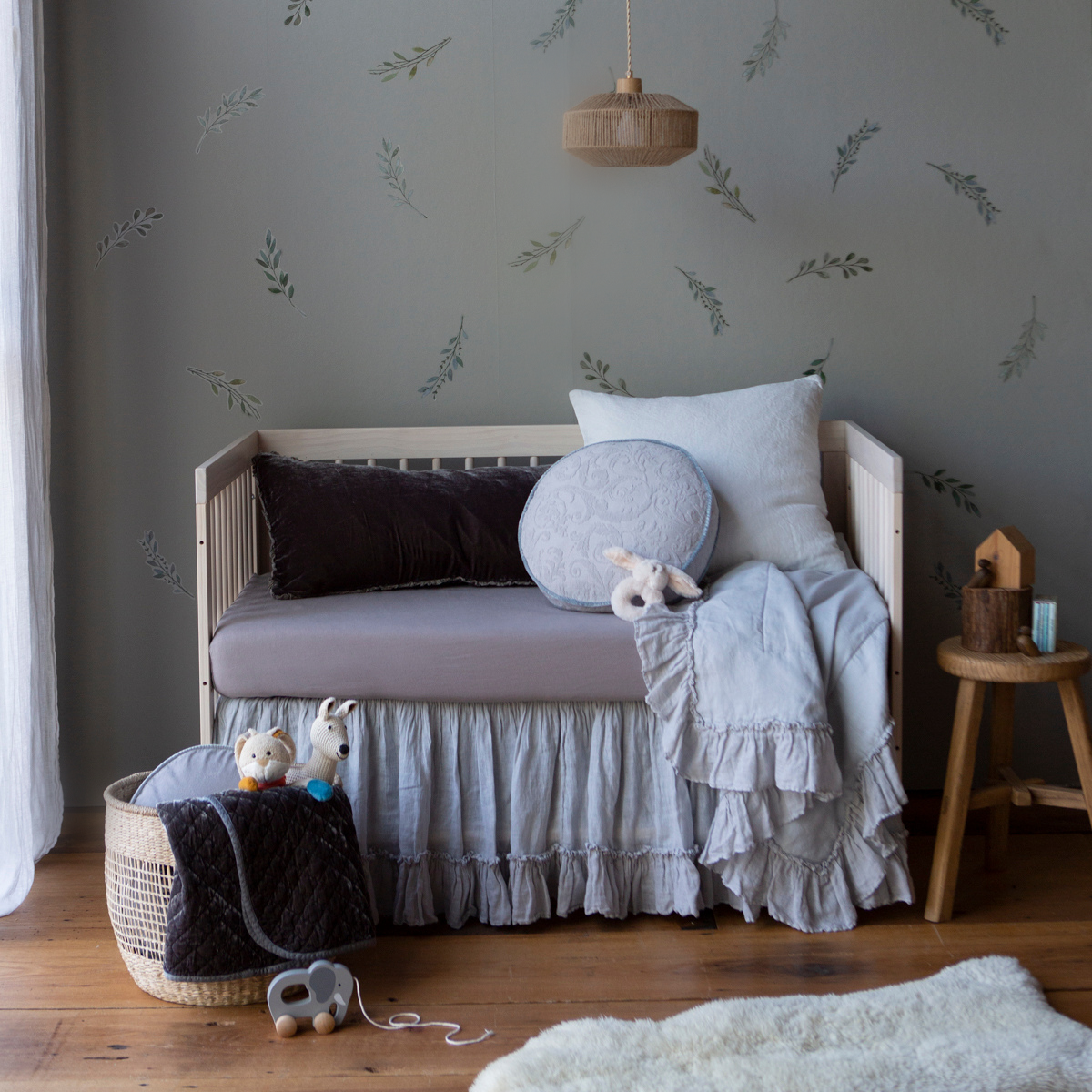 : Crib sheet in moonlight on a grey and light blue toned bed in a nursery with warm wood accents.