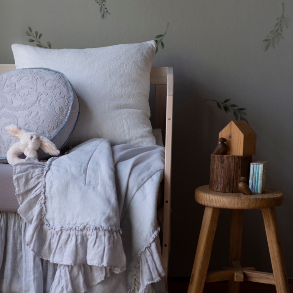 : Close up of blanket in cloud, draped over the front of a crib in other light blue and white tones, highlighting the ruffle trim.