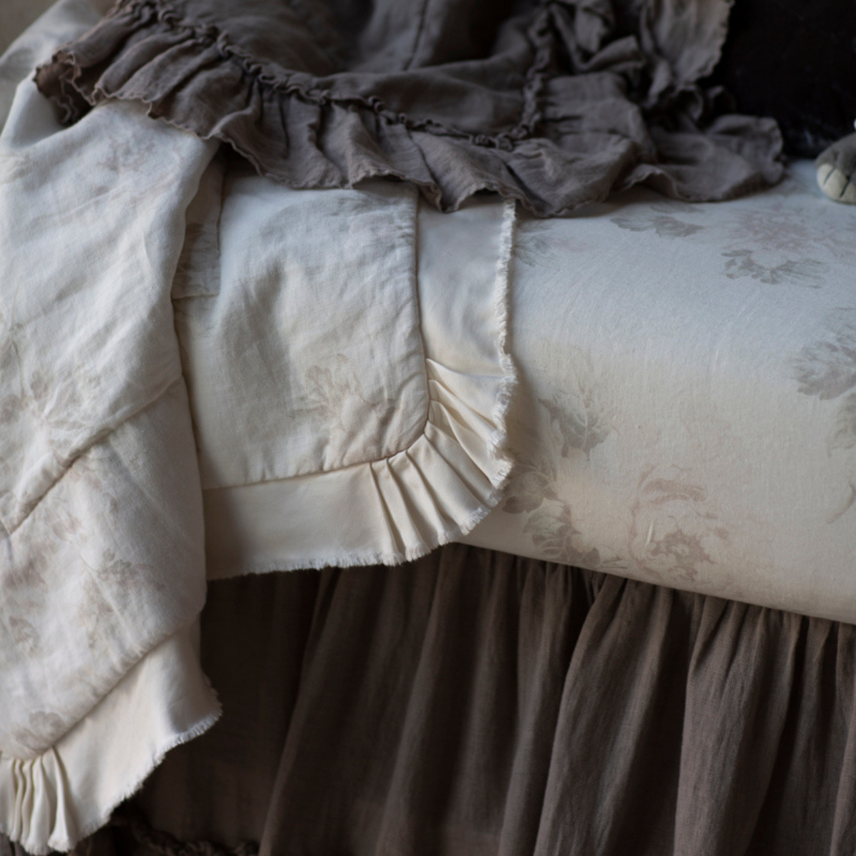 : Close up of blanket and crib sheet showcases the muted floral pattern of the linen and the satin trim detail.