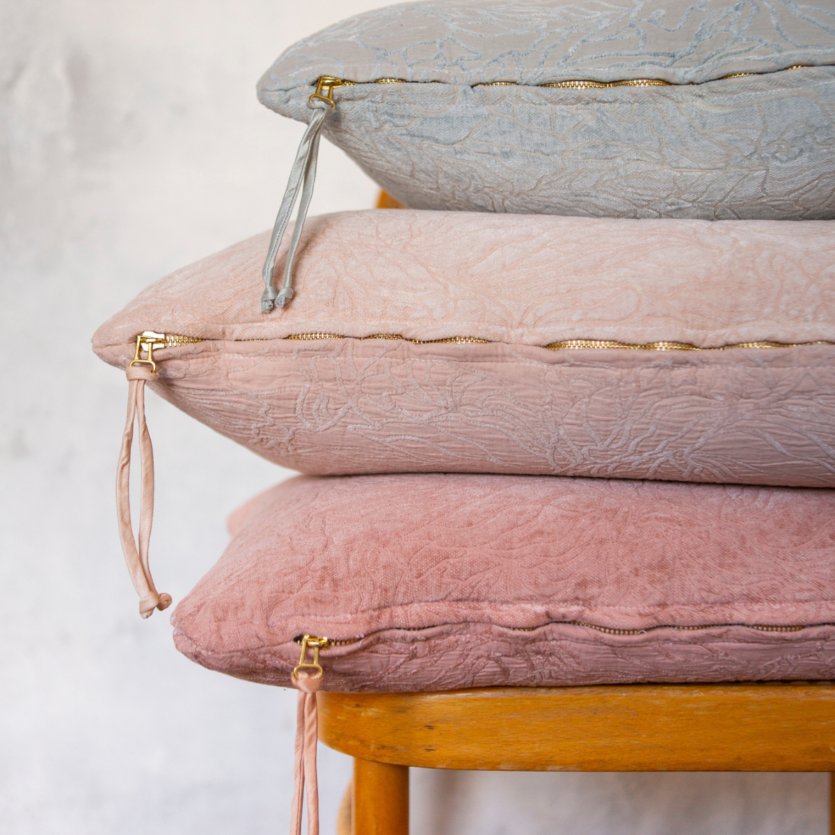 : light and warm colored throw pillows in cotton and chenille jacquard shown stacked against a light grey wall, somewhat closeup with the bottom zippers and pulls visible in the shot.