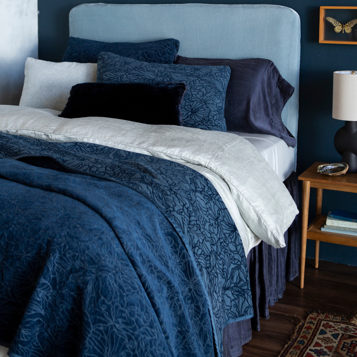 : shot at a three-quarter angle, the fully dressed bed is shown in blue tones in different fabrics showing the tonality and of the hues and pattern on the chenille and cotton jacquard bedspread and shams