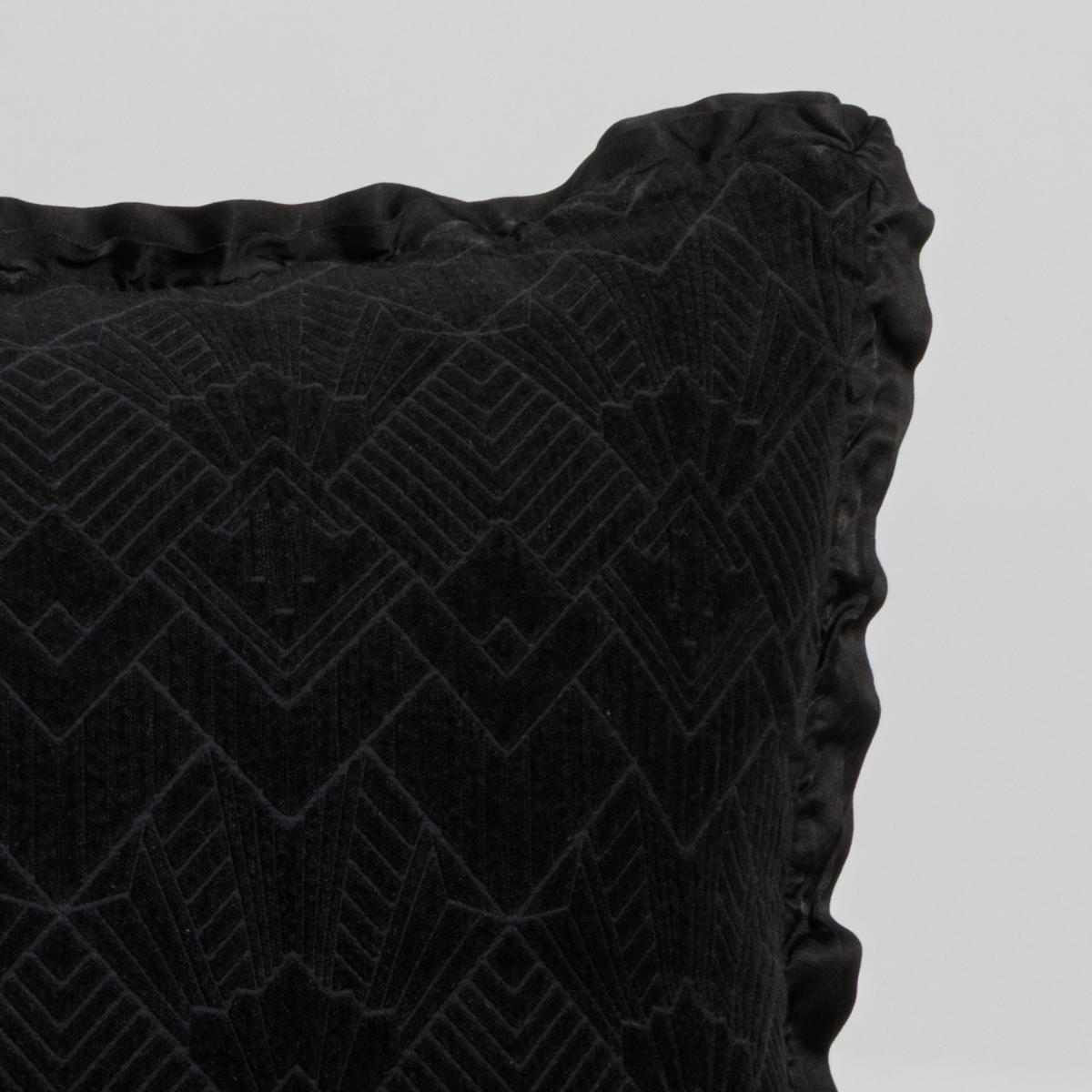 Corvino: Close-up of a textured pillow sham corner with a satin ruffle, shot against a plain background.