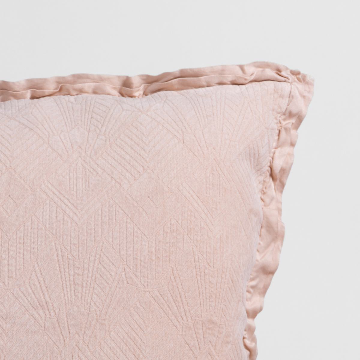 Pearl: Close-up of a textured pillow sham corner with a satin ruffle, shot against a plain background.