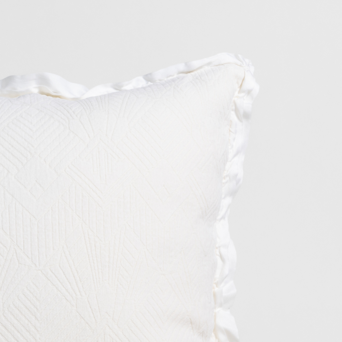Winter White: Close-up of a textured pillow sham corner with a satin ruffle, shot against a plain background.