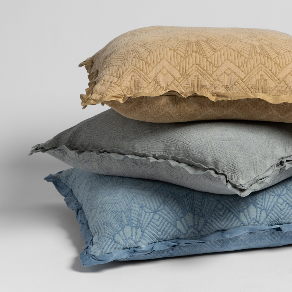 Stack of three patterned pillows in butterscotch-yellow, a midtone gray, and true blue on a plain, light background