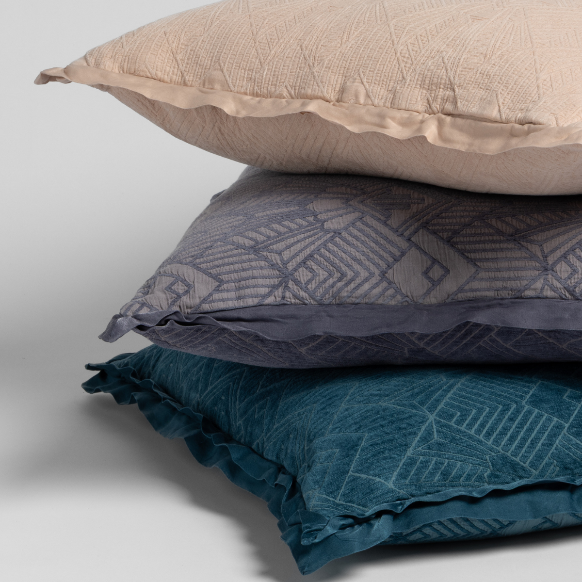Stack of three textured pillows in pearl, french lavender, and ccenote on a light background
