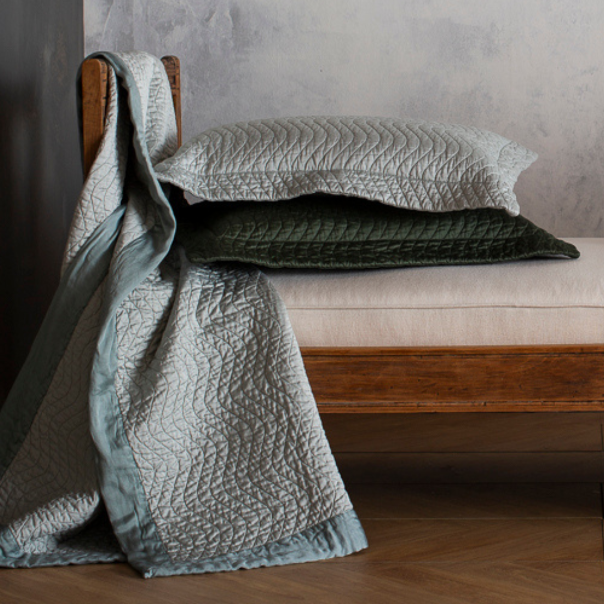 : pair of quilted cotton sateen throw pillows stacked on a daybed with matching throw blanket draped over its side.