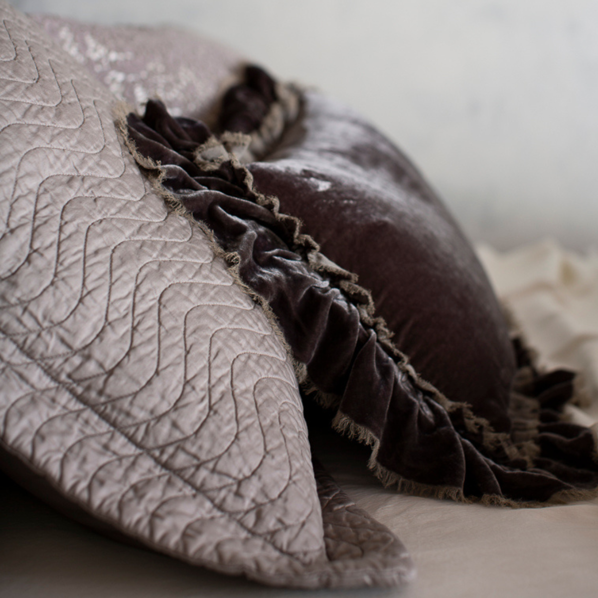 : close up of the side view of a quilted cotton sateen sham with silk velvet throw pillow with raw edges propped up against the pillow sham - both in grey tones.