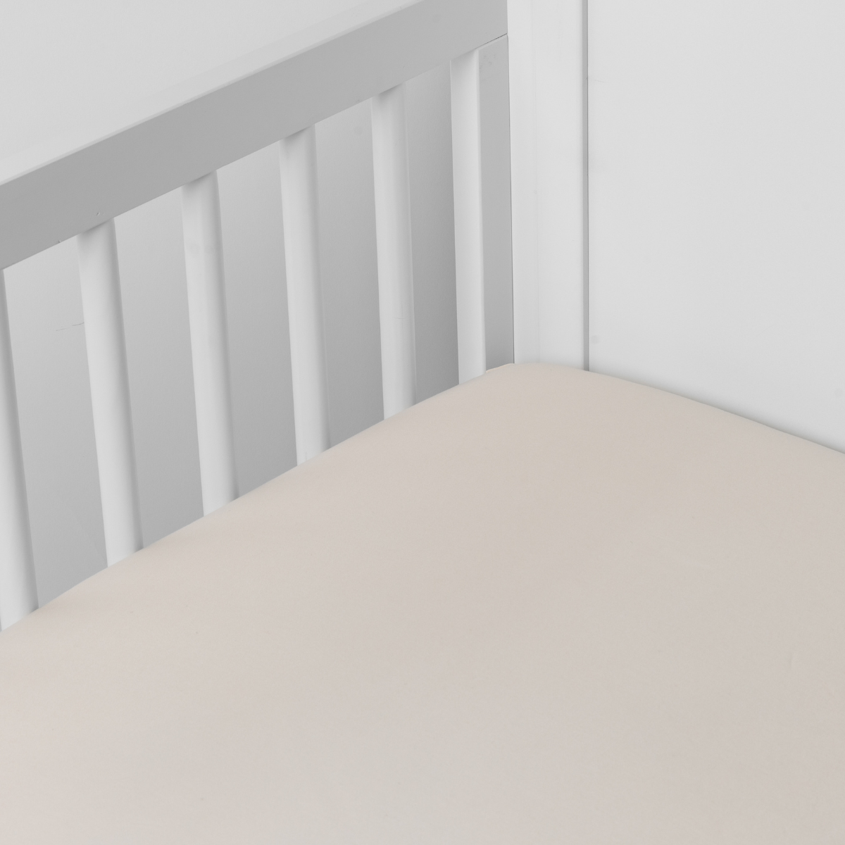 Parchment: Cotton sateen crib sheet shown from a slight overhead angle into an inside corner of a crib.