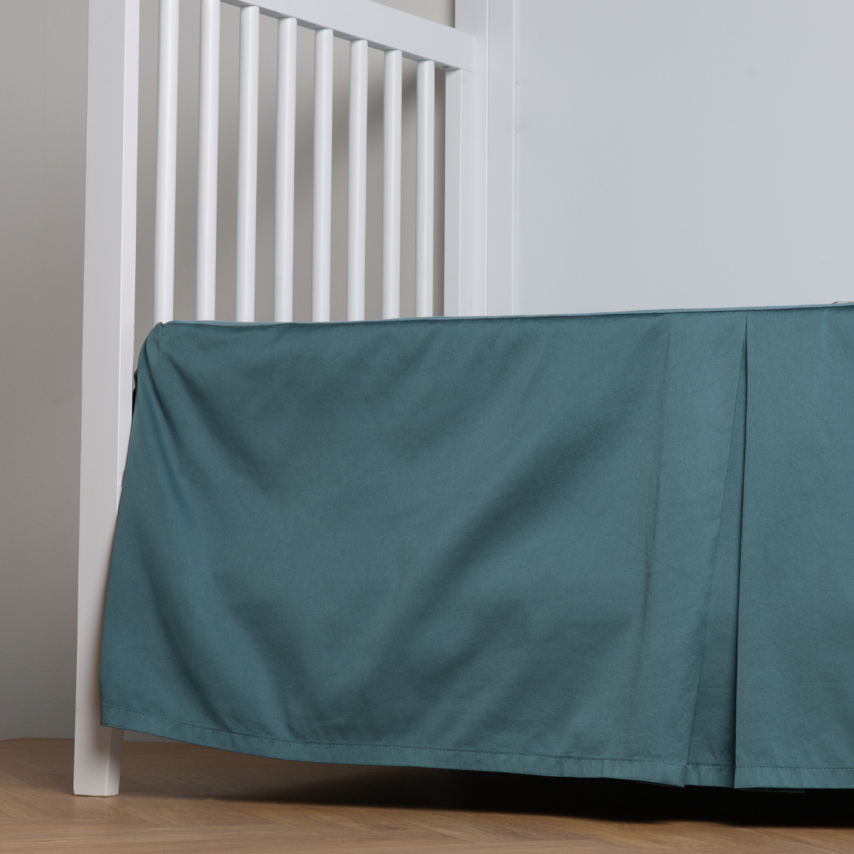 Cenote: cotton sateen cribi skirt with a center pleat shown straight on from a slight angle in a crib without a crib mattress.